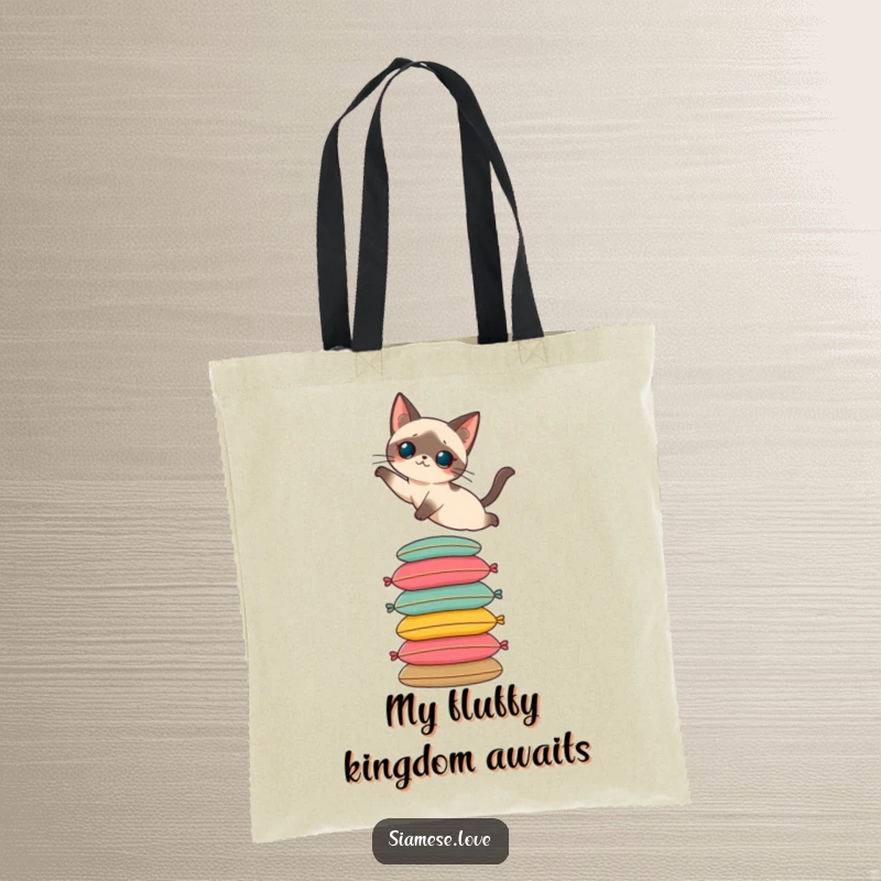 Funny tote bag featuring a Siamese cat elegantly leaping onto a colorful stack of cushions. Practical and chic.